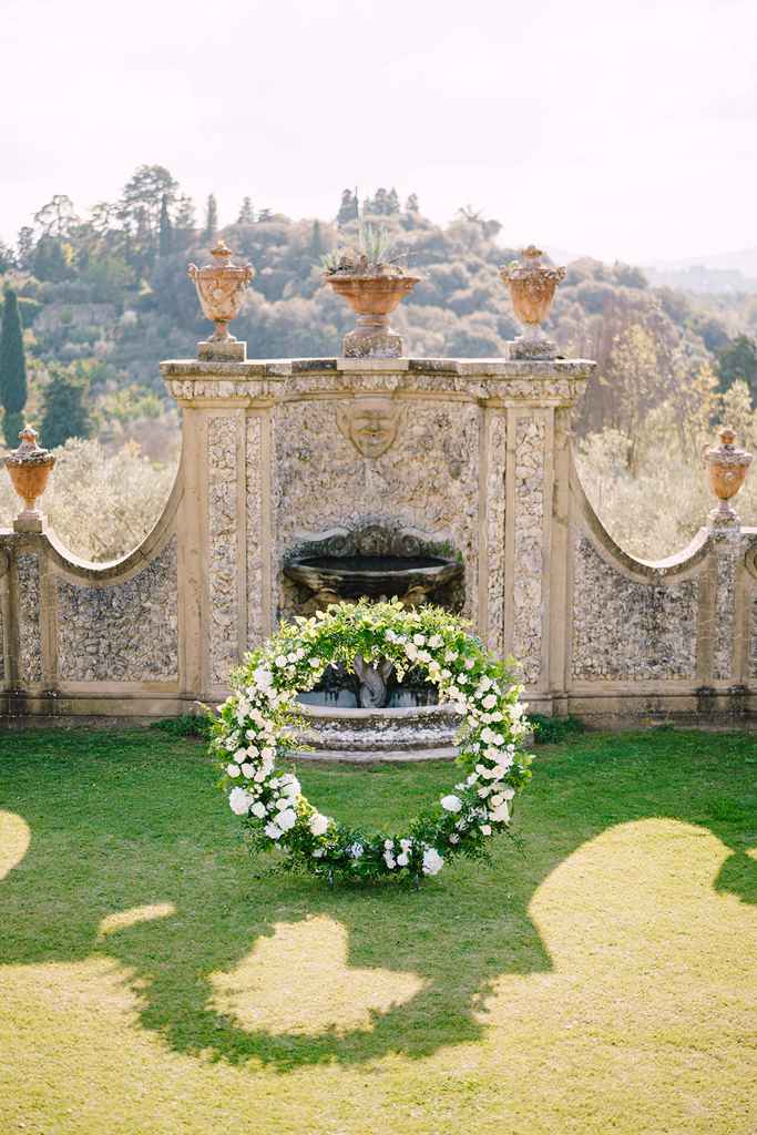 Prekrasen poročni obok z zelenjem in belimi cvetlicami, postavljen v sredini vrta. Foto: Storija weddings