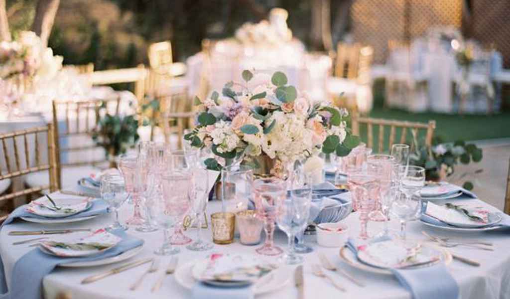 Poročna miza s cvetjem v pastelnih barvah, roza kozarci, srebrnim priborom ter roza in svetlo modrimi prtički. Foto: Esther Sun Photography